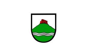 Das Wappen zeigt eine rote Burg auf einem grünen Hügel mit einer silbernen Wellenlinie darunter, alles umrahmt von einem schwarzen Rand.