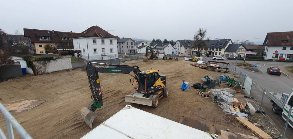 Eine Baustelle mit mehreren Baggern auf einem offenen, unbebauten Gelände, umgeben von Wohnhäusern.