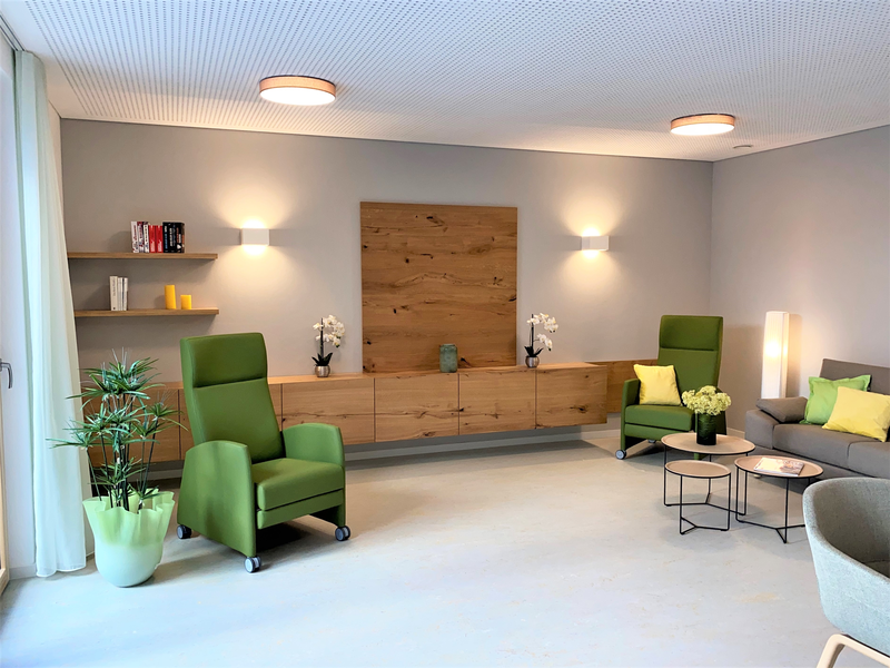 Ein modernes Wohnzimmer mit grünen Sesseln, dekorativen Pflanzen und Wandregalen, das eine einladende und gemütliche Atmosphäre schafft.