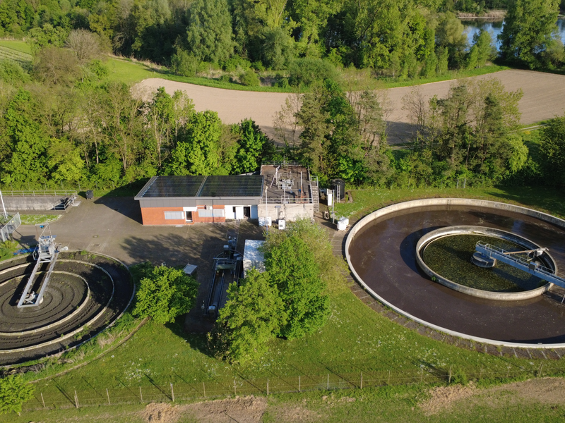 Luftaufnahme einer Kläranlage mit zwei runden Becken, umgeben von grünen Bäumen und Feldern.