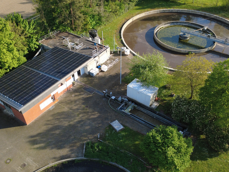 Luftaufnahme einer Kläranlage mit zwei runden Becken, umgeben von grünen Bäumen und Feldern.