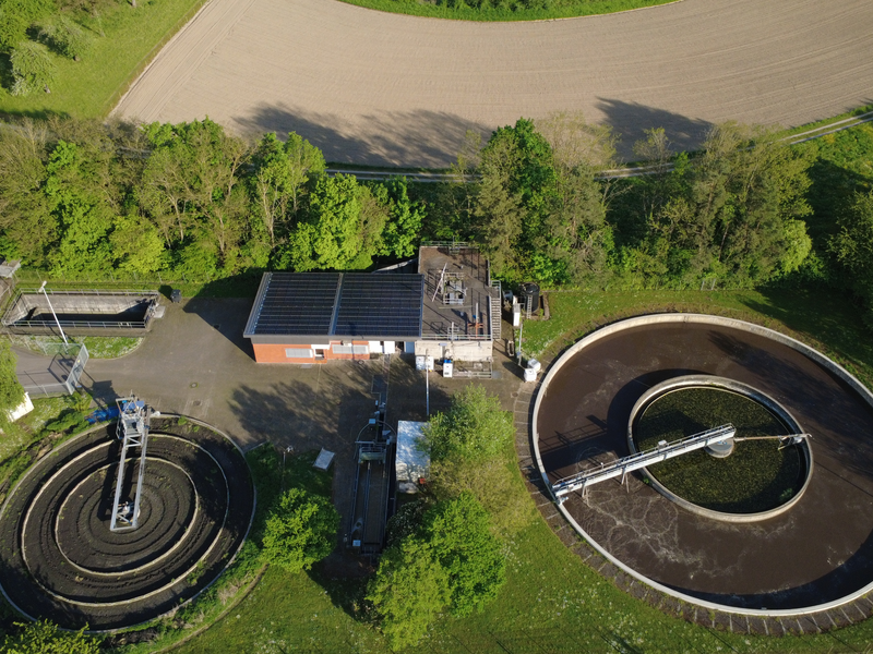 Luftaufnahme einer Kläranlage mit zwei runden Becken, umgeben von grünen Bäumen und Feldern.