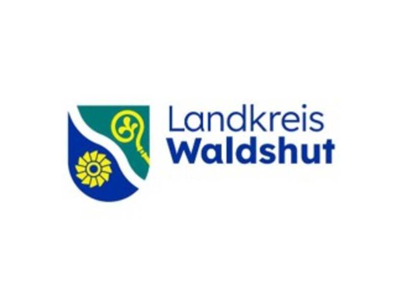links im Bild blaues Wappen, welches in der Mitte mit diagonalen Wellen getrennt ist, in der linken Hälfte ein gelbes Mühlrad oder Wasserrad und in der rechten Wappenhälfte ein gelbes Zepter, alles auf weißem Hintergrund, rechts im Bild ein blauer Schriftzug Landkreis Waldshut