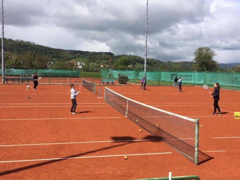  Tennisplatz mit mehreren Spielfelden, auf den einzelnen Spielfeldern sind Jugendliche und Erwachsene mit Tennisschlägern und Ball in Aktion
