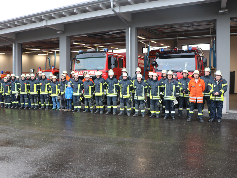 Gruppenfoto mit Mitgliedern der Freiwilligen Feuerwehr Küssaberg vor dem Feuerwehrhaus in Rheinheim mit geöffnetet Toren und dem Blick auf die darin stehenden Fahrzeuge im Hintergrund. 