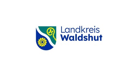 links im Bild blaues Wappen, welches in der Mitte mit diagonalen Wellen getrennt ist, in der linken Hälfte ein gelbes Mühlrad oder Wasserrad und in der rechten Wappenhälfte ein gelbes Zepter, alles auf weißem Hintergrund, rechts im Bild ein blauer Schriftzug Landkreis Waldshut